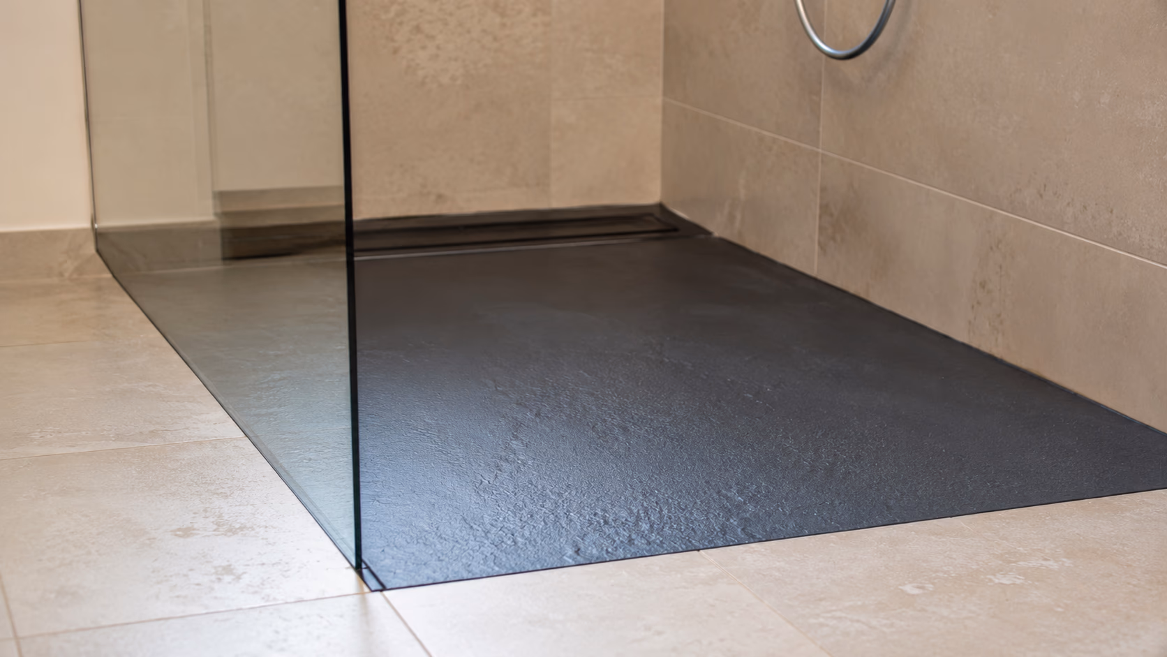 Détail d'un receveur extra-plat ardoise noire posé à niveau du carrelage avec siphon linéaire mural dans un appartement toulousain rénové